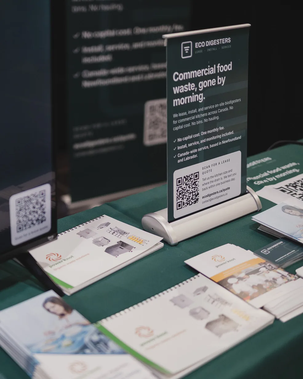 Our counter sign on the booth table, reading Commercial food waste, gone by morning. with a code to scan for a lease quote, beside Power Knot brochures.
